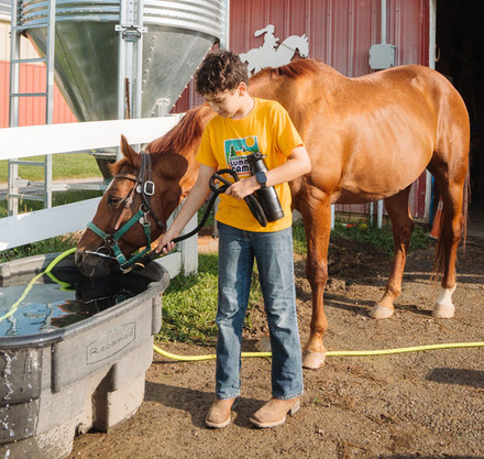 a boy holding binoculars and drinking water from a trough