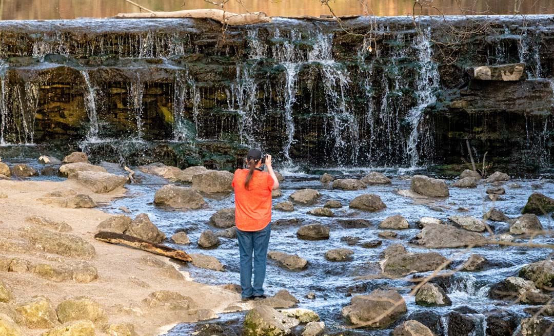 a woman taking a picture of a waterfall